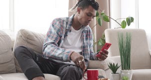 Sirva desayunar mientras que usa el teléfono móvil en el sofá almacen de video Sirva desayunar mientras que usa el teléfono móvil en el sofá almacen de video