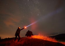 Situaci?n de la mujer contra el cielo estrellado de la noche en las monta?as con una linterna en su mano imagenes de archivo Situaci?n de la mujer contra el cielo estrellado de la noche en las monta?as con una linterna en su mano imagenes de archivo