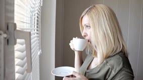 Situaci?n rubia hermosa thinkful triste joven de la mujer cerca de la ventana con las persianas por la ma?ana y el caf? de consum metrajes Situaci?n rubia hermosa thinkful triste joven de la mujer cerca de la ventana con las persianas por la ma?ana y el caf? de consum metrajes