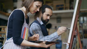 Skilled artist man teaching young woman painting on easel at art school studio - creativity, education and art people stock photo Skilled artist man teaching young woman painting on easel at art school studio - creativity, education and art people stock photo