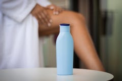 Skin care during summer concept: close-up a bottle of cream and woman applying body lotion on her legs stock photo Skin care during summer concept: close-up a bottle of cream and woman applying body lotion on her legs stock photo