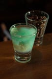 Skjutit exponeringsglas med den blåa alkoholdrinken nära exponeringsglas med kaffebönor arkivfoton Skjutit exponeringsglas med den blåa alkoholdrinken nära exponeringsglas med kaffebönor arkivfoton