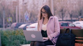 Skoncentrowana atrakcyjna kobieta używa laptop w parku podczas gdy siedzący na ławce zbiory wideo Skoncentrowana atrakcyjna kobieta używa laptop w parku podczas gdy siedzący na ławce zbiory wideo