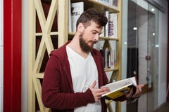 Skoncentrowany facet trzyma szkła i czytelniczą książkę w bibliotece fotografia stock Skoncentrowany facet trzyma szkła i czytelniczą książkę w bibliotece fotografia stock
