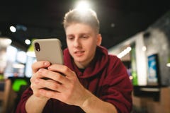 Skupia się na smartphone, pozytywny facet używa internet na smartphone Młody człowiek używa smartphone w fast food kawiarni obraz stock Skupia się na smartphone, pozytywny facet używa internet na smartphone Młody człowiek używa smartphone w fast food kawiarni obraz stock
