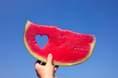 A slice of watermelon and heart against the bright summer sky in the girl`s hand. stock photos A slice of watermelon and heart against the bright summer sky in the girl`s hand. stock photos