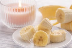 Sliced banana on a white plate and a light wooden table. Pink burning candle nearby stock photos Sliced banana on a white plate and a light wooden table. Pink burning candle nearby stock photos