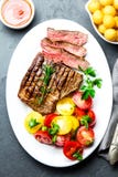 Sliced medium rare grilled beef steak served on white plate with tomato salad and potatoes balls. Barbecue, bbq meat stock image Sliced medium rare grilled beef steak served on white plate with tomato salad and potatoes balls. Barbecue, bbq meat stock image