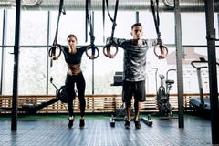 Slim girl dressed black sports clothes and athletic man are doing exercises on gymnastic rings in the gym royalty free stock images Slim girl dressed black sports clothes and athletic man are doing exercises on gymnastic rings in the gym royalty free stock images