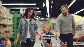 Slow motion of happy family father, mother and child running through supermarket with shopping cart, smiling and stock video Slow motion of happy family father, mother and child running through supermarket with shopping cart, smiling and stock video