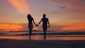 Slow motion silhouette of happy loving couple meet and go to beach on sunset in ocean shore stock video Slow motion silhouette of happy loving couple meet and go to beach on sunset in ocean shore stock video