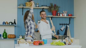 Slowmotion of Young joyful couple have fun dancing and singing while cooking in the kitchen at home