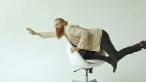 Slowmotion of Bearded funny businessman have fun riding on office chair on white background