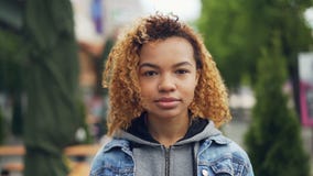 Slowmotion portrait of pretty African American girl modern teenager looking at camera and smiling while standing in