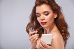 Sluit omhoog portret van aantrekkelijk meisje die haar lippen rouging Zij houdt rode lippenstift in de muis Geïsoleerd op grijs royalty-vrije stock fotografie Sluit omhoog portret van aantrekkelijk meisje die haar lippen rouging Zij houdt rode lippenstift in de muis Geïsoleerd op grijs royalty-vrije stock fotografie