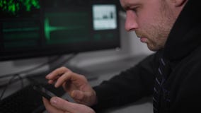 Sluit omhoog van Russische hakkerzitting bij de lijst en het gebruiken van zijn smartphone De mannelijke spion binnendringt in ee stock footage Sluit omhoog van Russische hakkerzitting bij de lijst en het gebruiken van zijn smartphone De mannelijke spion binnendringt in ee stock footage