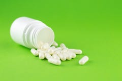 Sluit omhoog witte pillenfles met gemorste uit capsules op groene achtergrond met exemplaarruimte Nadruk op voorgrond, zachte bok stock fotografie Sluit omhoog witte pillenfles met gemorste uit capsules op groene achtergrond met exemplaarruimte Nadruk op voorgrond, zachte bok stock fotografie