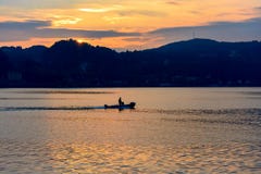 Small boat floating on the water at sunset against the backdrop of mountains and the setting sun. royalty free stock images Small boat floating on the water at sunset against the backdrop of mountains and the setting sun. royalty free stock images
