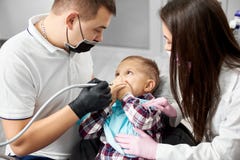 A small child is covering his mouth being scared because of the dental treatment carried out by a male dentist stock image A small child is covering his mouth being scared because of the dental treatment carried out by a male dentist stock image