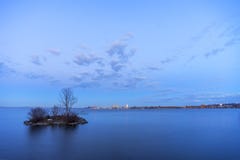 Small island in smooth lake at dusk hiding a nesting swan, safely removed from vibrant cityscape in the distance across the water royalty free stock image Small island in smooth lake at dusk hiding a nesting swan, safely removed from vibrant cityscape in the distance across the water royalty free stock image