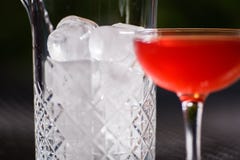 A small low glass with a red alcoholic cocktail is on the table next to a glass vase full of large square pieces of clear ice. Against a background of Royalty Free Stock Images A small low glass with a red alcoholic cocktail is on the table next to a glass vase full of large square pieces of clear ice. Against a background of Royalty Free Stock Images