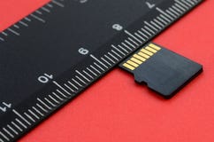 Small micro SD memory card lie on a red background next to a black ruler. A small and compact data and information store Stock Image Small micro SD memory card lie on a red background next to a black ruler. A small and compact data and information store Stock Image