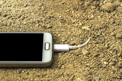 Smartphone blanc avec un chargeur branché au sable fond avant et arrière brouillé photos libres de droits Smartphone blanc avec un chargeur branché au sable fond avant et arrière brouillé photos libres de droits
