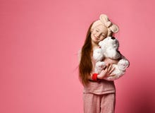 Smiling baby girl holding a white teddy bear in the room a pink backdrop.
