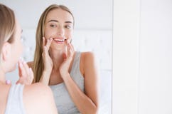 Smiling beautiful young woman looking into a mirror at herself in room. Beauty, hygiene, morning and people concept royalty free stock photography Smiling beautiful young woman looking into a mirror at herself in room. Beauty, hygiene, morning and people concept royalty free stock photography