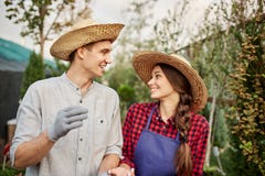 Smiling guy and girl gardeners in a straw hats look to each other in garden on a sunny day. royalty free stock photo Smiling guy and girl gardeners in a straw hats look to each other in garden on a sunny day. royalty free stock photo