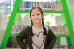 Smiling Little Asian Child Girl Against Bookshelf At Library. Children Creativity And Imagination Concept Royalty Free Stock Photo