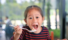 Smiling Little Asian Child Girl Sitting At The Cafe And Eating Food With Looking Straight Royalty Free Stock Image Smiling Little Asian Child Girl Sitting At The Cafe And Eating Food With Looking Straight Royalty Free Stock Image