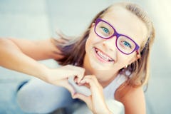 Smiling Little Girl In With Braces And Glasses Showing Heart With Hands Stock Photo Smiling Little Girl In With Braces And Glasses Showing Heart With Hands Stock Photo