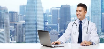 Smiling male doctor with laptop sitting at table royalty free stock photo Smiling male doctor with laptop sitting at table royalty free stock photo