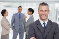 Smiling manager posing with employees in background. In bright office Smiling manager posing with employees in background. In bright office