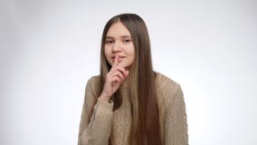 Smiling teenage girl making silent gesture with finger at mouth after telling secret information