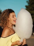 Smiling woman with curly hair has fun with cotton candy outdoors.