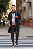 Smiling young hipster mixed race guy standing on the street, holding a backpack on shoulder and looking at camera. stock photos Smiling young hipster mixed race guy standing on the street, holding a backpack on shoulder and looking at camera. stock photos