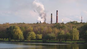 Smoke of factory pipes near a forest and river .