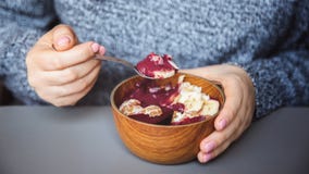 Smoothie Acai, granola, семена, свежие фрукты в деревянном шаре в женских руках на серой таблице Еда здорового шара завтрака стоковое фото rf Smoothie Acai, granola, семена, свежие фрукты в деревянном шаре в женских руках на серой таблице Еда здорового шара завтрака стоковое фото rf
