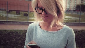 Smutna młodej kobiety pozycja w parkowym terenie wśród buldings używać jej smartphone texting czuć smutny zbiory Smutna młodej kobiety pozycja w parkowym terenie wśród buldings używać jej smartphone texting czuć smutny zbiory