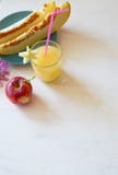 Snijd de meloen naast de rode appelen, een glas van smoothie met een plak van meloen met een stro royalty-vrije stock foto Snijd de meloen naast de rode appelen, een glas van smoothie met een plak van meloen met een stro royalty-vrije stock foto