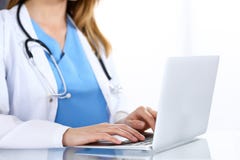 Soignez la dactylographie sur l'ordinateur portable tout en se reposant au bureau en verre dans le bureau d'hôpital Médecin au tr image stock Soignez la dactylographie sur l'ordinateur portable tout en se reposant au bureau en verre dans le bureau d'hôpital Médecin au tr image stock