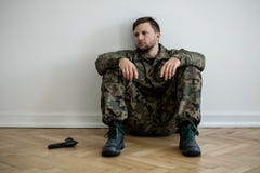 Soldat professionnel fatigué dans l'uniforme vert se reposant sur le plancher à côté d'une arme à feu images libres de droits Soldat professionnel fatigué dans l'uniforme vert se reposant sur le plancher à côté d'une arme à feu images libres de droits