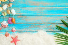 Sommerhintergrund mit dem Strandsand, starfishs Kokosnussblättern und Oberteildekoration, die am blauen hölzernen Hintergrund hän Sommerhintergrund mit dem Strandsand, starfishs Kokosnussblättern und Oberteildekoration, die am blauen hölzernen Hintergrund hän