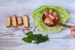 A sopa cozinhada no caldo da carne com ervas e o pão torrado frescos é derramada em uma placa com folha da couve imagem de stock royalty free A sopa cozinhada no caldo da carne com ervas e o pão torrado frescos é derramada em uma placa com folha da couve imagem de stock royalty free