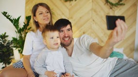 Sorrir parents com o bebê que toma a foto de família do selfie na cama em casa Imagem de Stock Royalty Free Sorrir parents com o bebê que toma a foto de família do selfie na cama em casa Imagem de Stock Royalty Free
