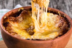 Soupe française à gratin d'oignon dans un pot d'argile, recette authentique, cuillère en bois sur une planche à découper sur une photographie stock Soupe française à gratin d'oignon dans un pot d'argile, recette authentique, cuillère en bois sur une planche à découper sur une photographie stock