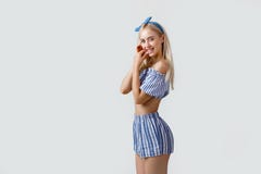 Spielerisches schönes blondes Mädchen in der Sommerausstattung, lächelnd und werfen an der Kamera auf und stehen über weißem Hint stockfotografie Spielerisches schönes blondes Mädchen in der Sommerausstattung, lächelnd und werfen an der Kamera auf und stehen über weißem Hint stockfotografie
