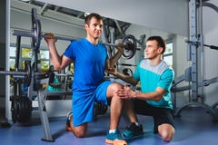 Sport, fitness, teamwork, bodybuilding people concept - man and personal trainer with barbell flexing muscles in gym